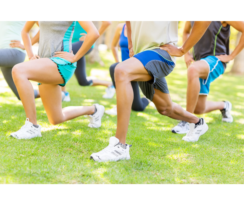 A group of individuals engaging in a fitness class outdoors, performing lunges on the grass in a park setting, dressed in athletic gear on a bright, sunny day.
