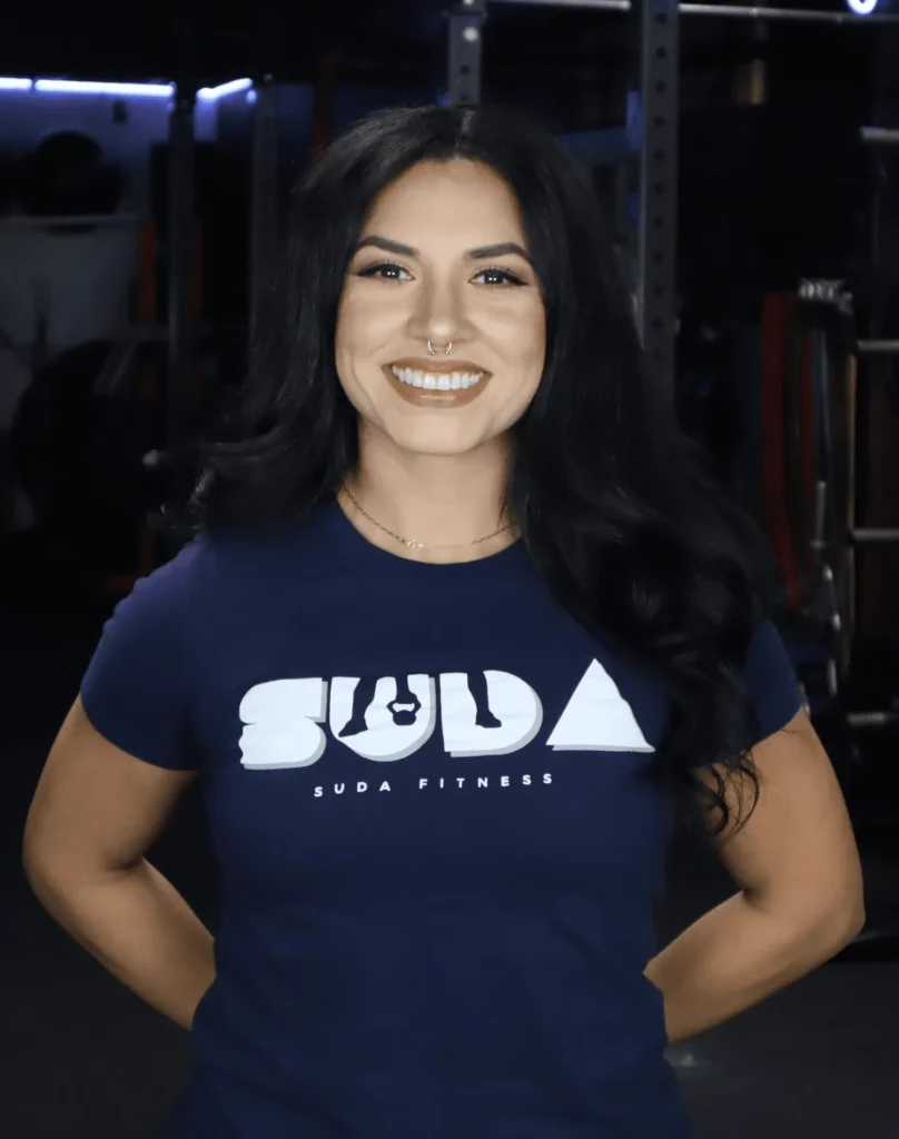 Alejandra Hernandez, certified personal trainer at SUDA Fitness, standing confidently in a modern gym wearing a branded training shirt.