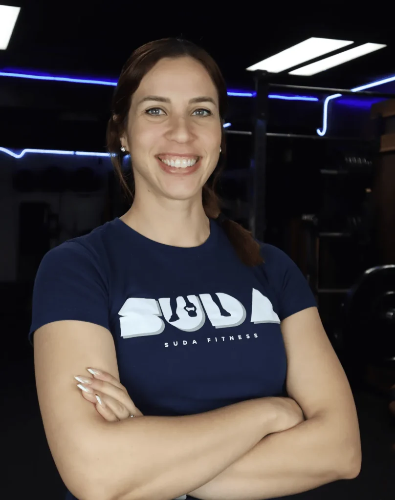 Karen Polo, certified personal trainer at SUDA Fitness, smiling with arms crossed inside a professional gym environment.