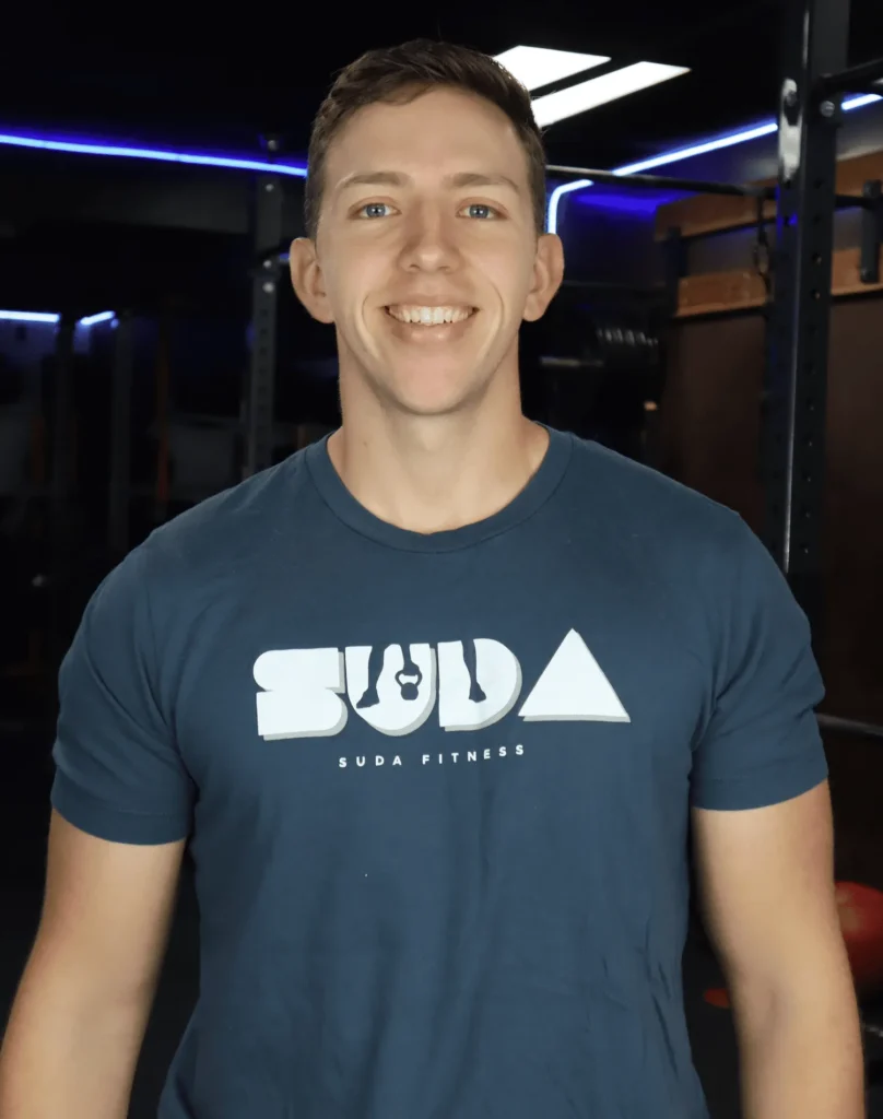 Luis Sanchez, certified personal trainer at SUDA Fitness, standing in a gym wearing a SUDA Fitness t-shirt and smiling confidently.